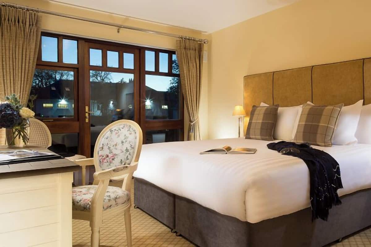 A hotel room with a large bed, a desk, a chair, and a nightstand.