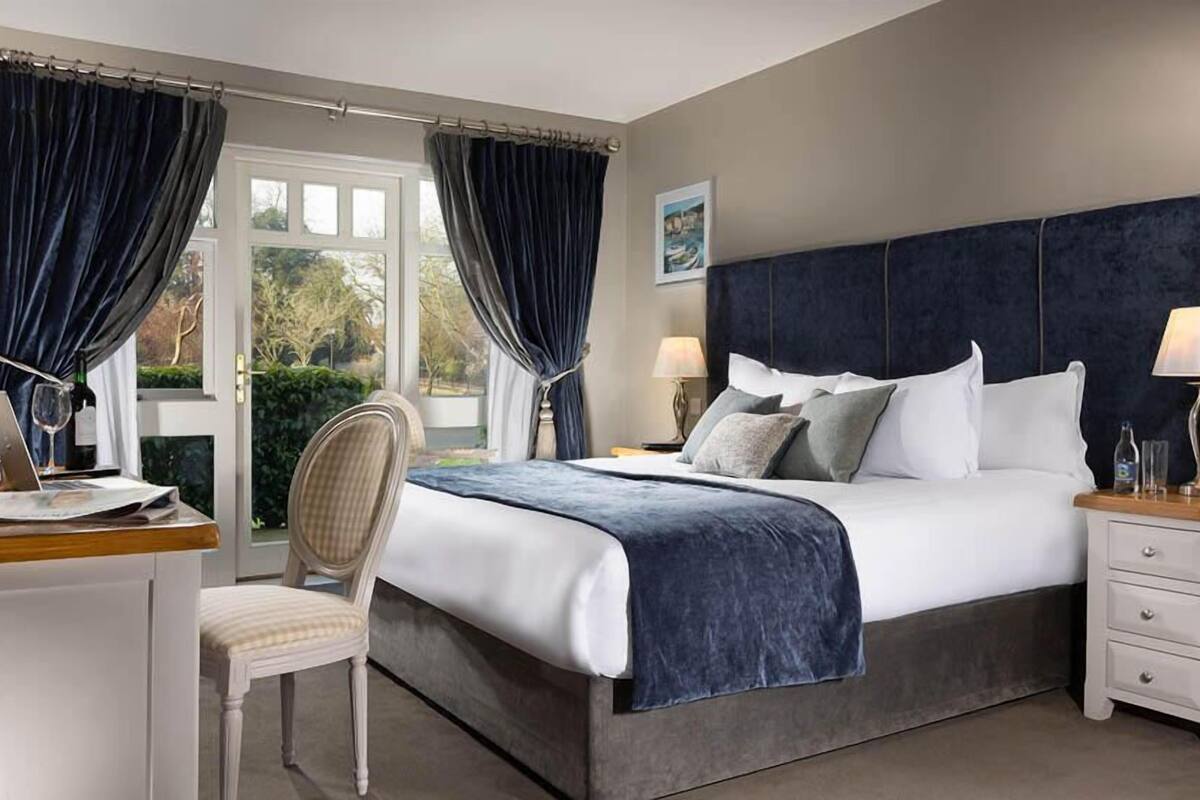 A bedroom with a large bed, two bedside tables with lamps, a chair, and a desk with a laptop and a wine glass.