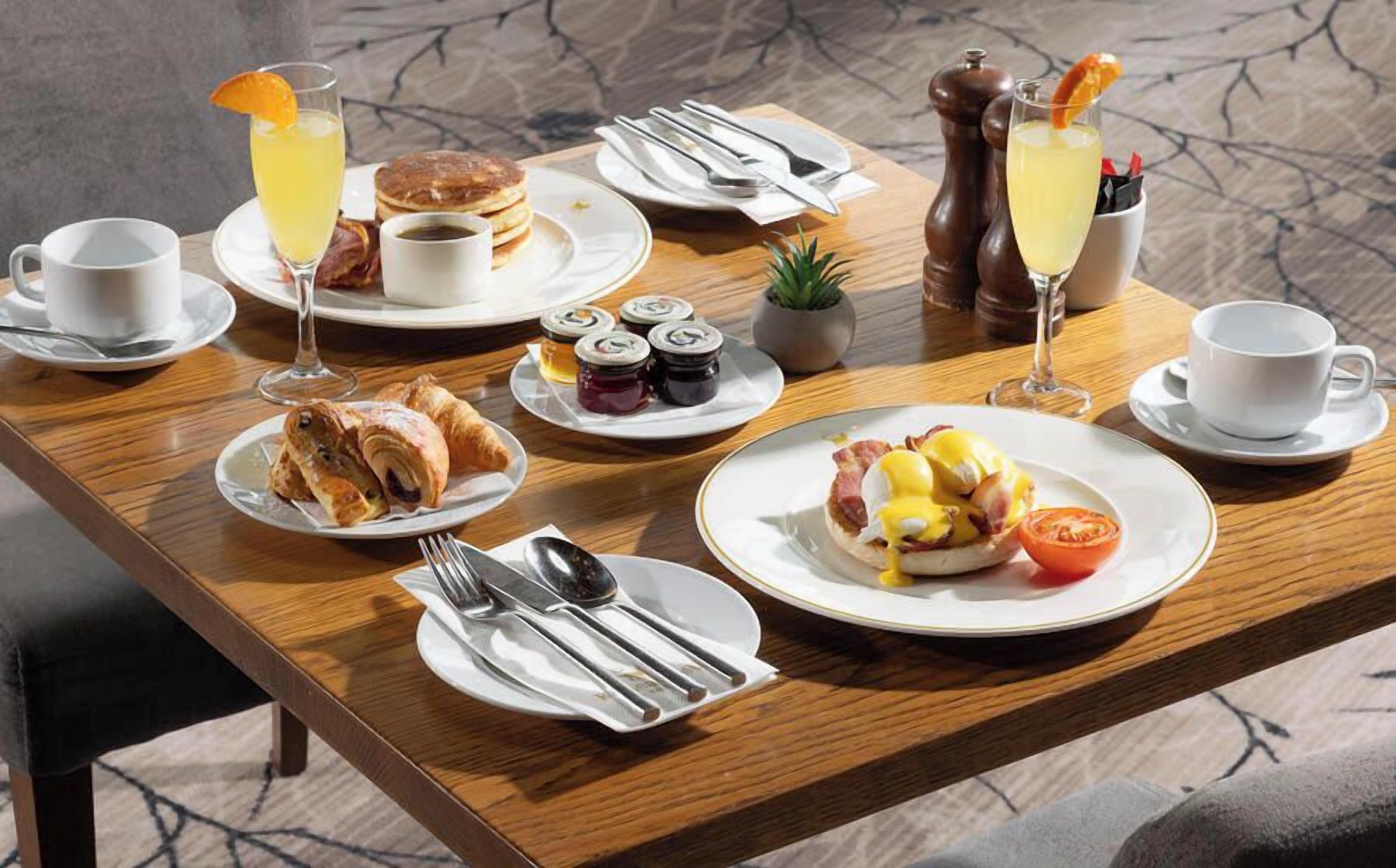 Taula de l'esmorzar amb diferents plats, incloent creps, croissants i ous Benedict, acompanyats de tasses i un got de suc d'aranja.