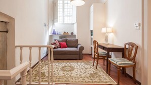 A cozy living room with a sofa, a dining table, and chairs. There's a patterned rug on the floor. - Suite Elda (Verona)