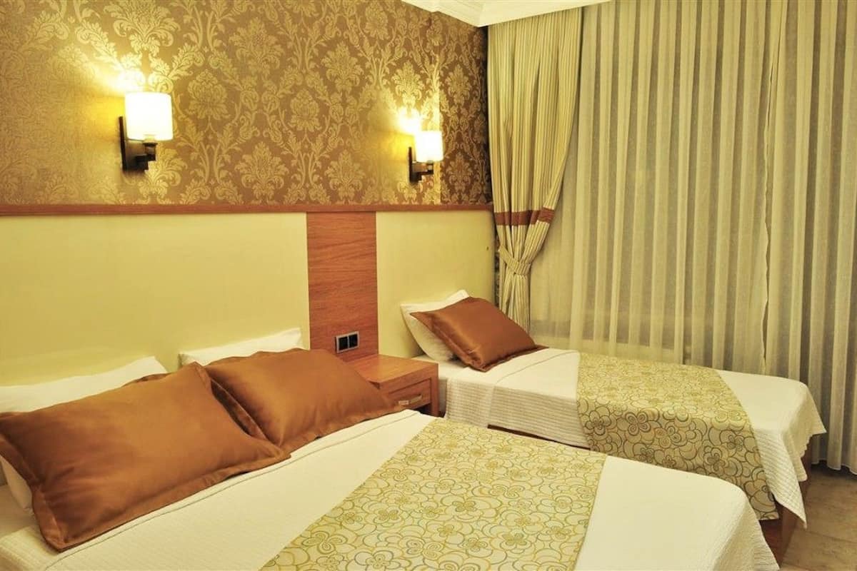 Habitación de hotel con dos camas, cabecero de madera, papel tapiz estampado y cortina.