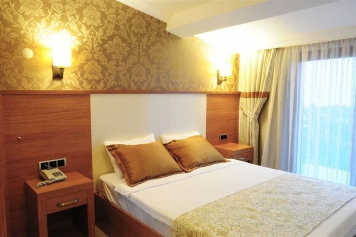 A hotel room with a large bed, two bedside tables, a telephone, and patterned wallpaper.