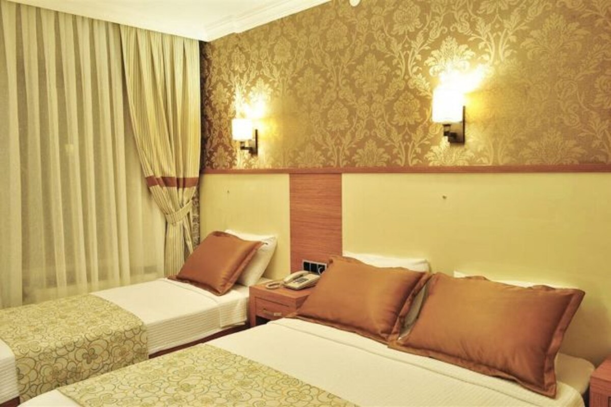 A hotel room with two beds, a wooden headboard, a telephone, and two wall-mounted lights.