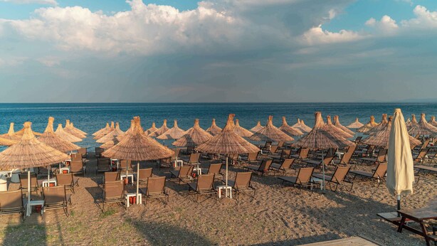 A beach with rows of sun loungers and thatched umbrellas, facing the sea. - Assos Park Hotel (Ayvacik)
