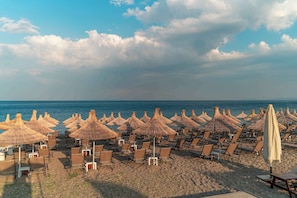A beach with rows of sun loungers and thatched umbrellas, facing the sea. - Assos Park Hotel (Ayvacik)