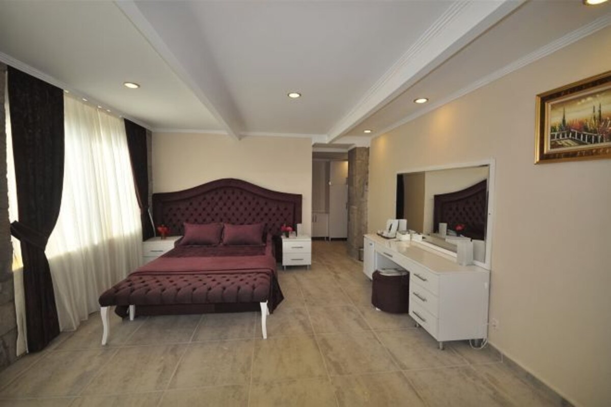 A bedroom with a large bed, bedside tables, a vanity with a mirror, and a painting on the wall.