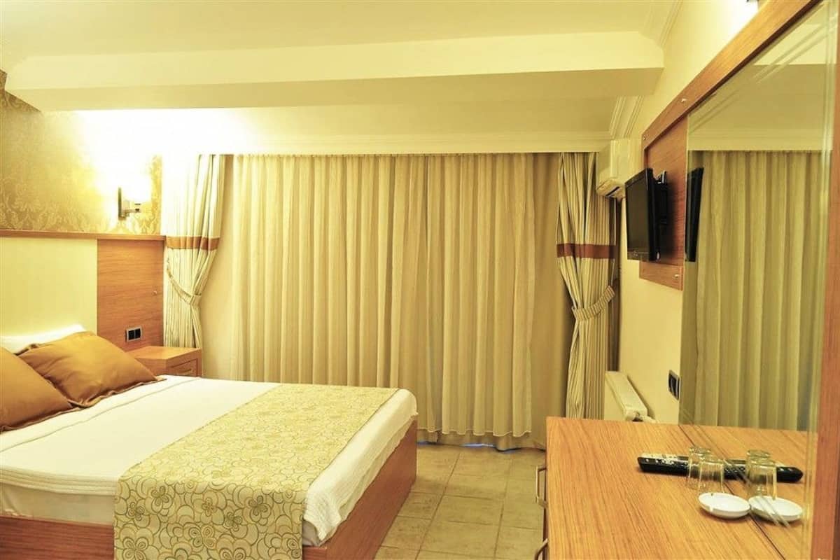 Habitación de hotel con cama, mesita de noche, televisor y espejo.