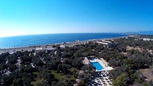 An aerial view of a coastal resort with a swimming pool surrounded by lounge chairs, a beach, and dense vegetation. - Assos Park Hotel (Ayvacik)