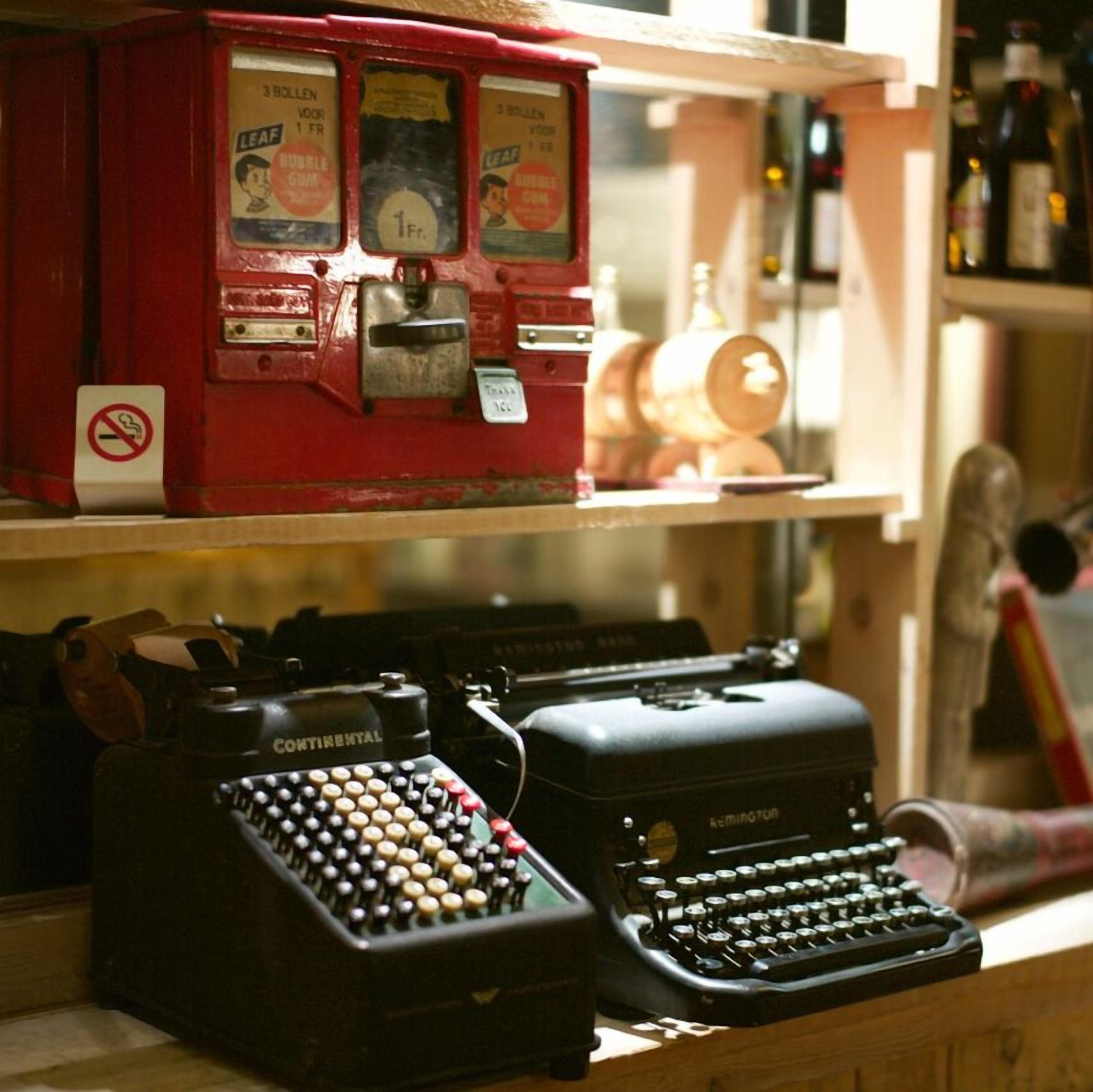 A shelf with vintage typewriters and a red vending machine.