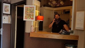 A hotel reception area with a counter, a mirror, a telephone, a menu board, and a bar stool. - Hostel Galia (Brussels)