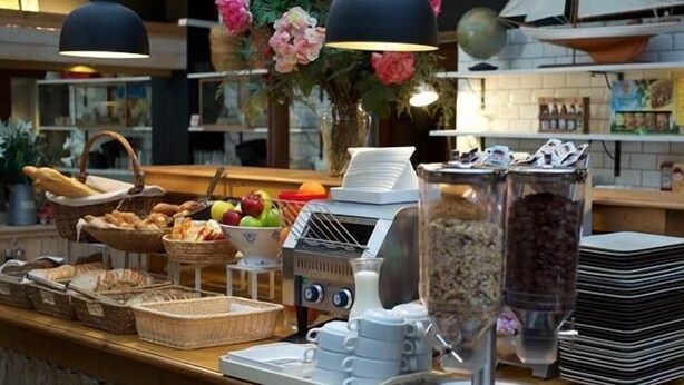 A breakfast buffet with various food items, a coffee machine, and decorative flowers. - Hostel Galia (Brussels)