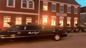 Un lujoso coche de alquiler negro estacionado frente a un hotel de estilo arquitectónico clásico, con amplias ventanas y un cartel que indica que es un hotel.