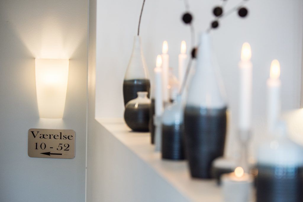 Un pasillo con un cartel que indica la habitación número 10-52, una lámpara de pared y varias velas sobre una mesa.