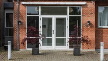 Ein Gebäude mit Ziegelwand, großen Glasfenstern und Pflanzen im Topf vor der Fassade.