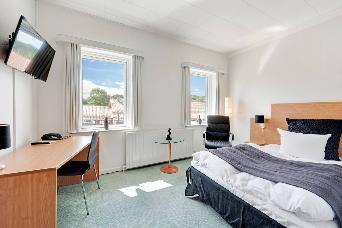 Une chambre d’hôtel équipée d’un lit, d’un bureau, d’une chaise, d’une télévision et de fenêtres.