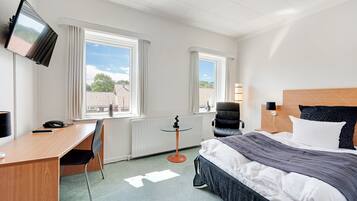 Een hotelkamer met een bed, bureau, stoel, televisie en ramen.
