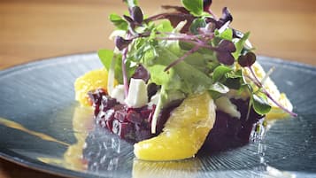 Une assiette contenant une salade composée de différentes feuilles, de betteraves et de tranches d’orange.