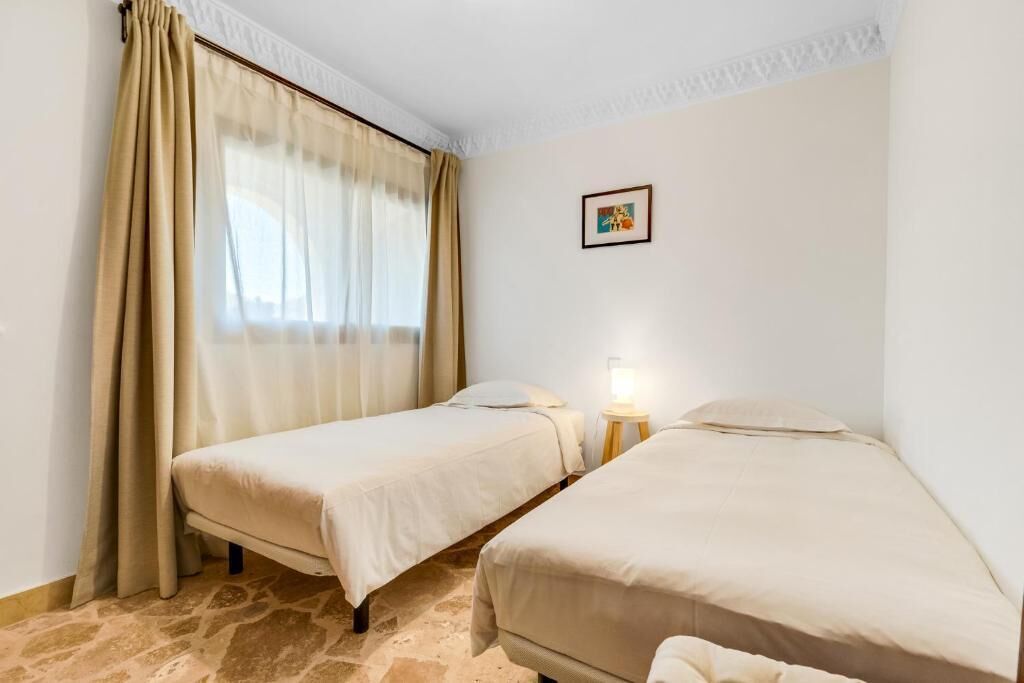 Una habitación con dos camas individuales, una mesita de noche con lámpara y un cuadro en la pared.