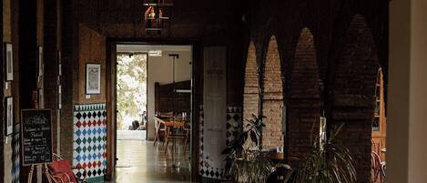 A spacious corridor with a high ceiling, potted plants, and a view into a dining area.