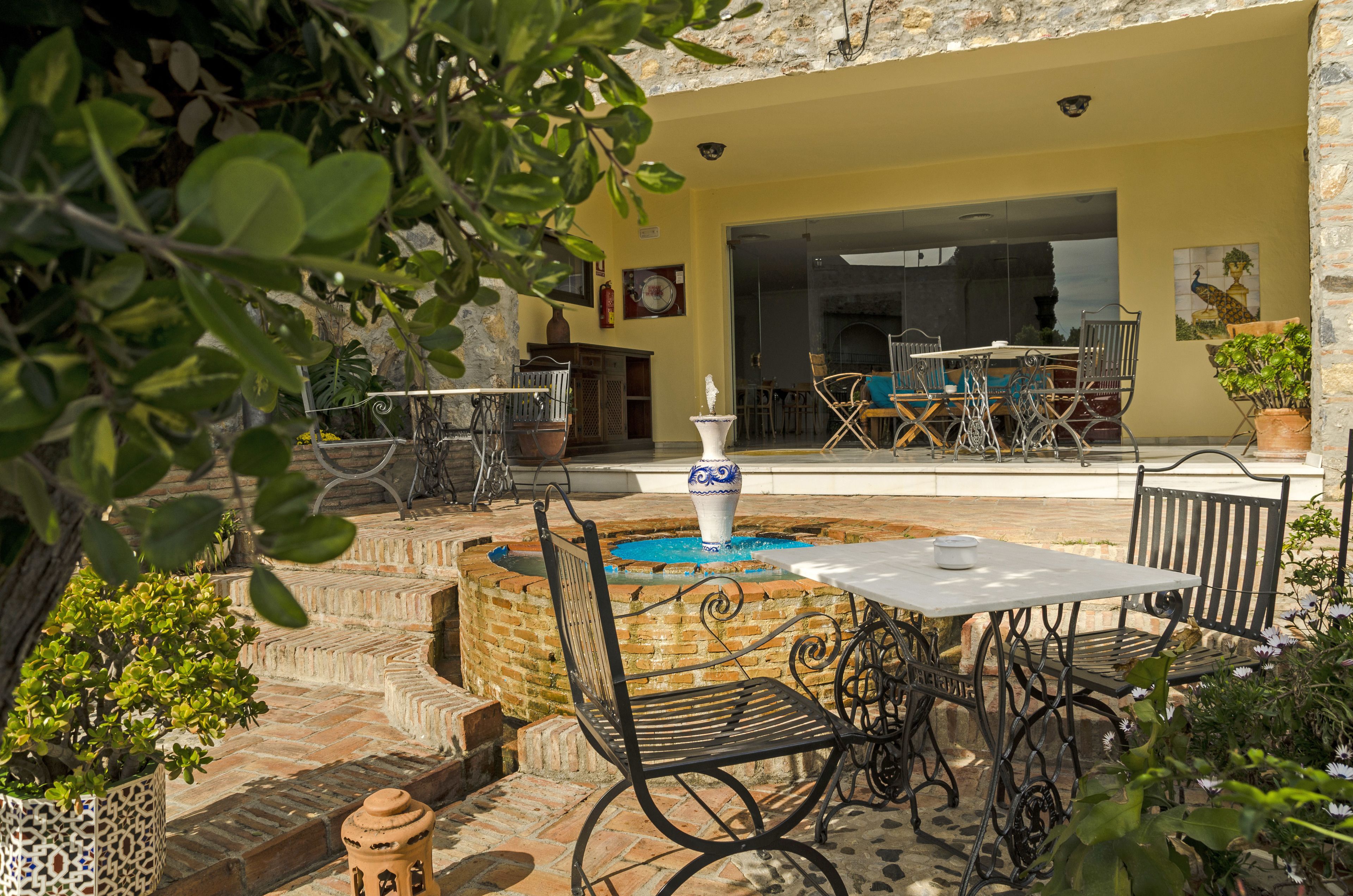An outdoor patio with a table and chairs, a fountain, and potted plants.
