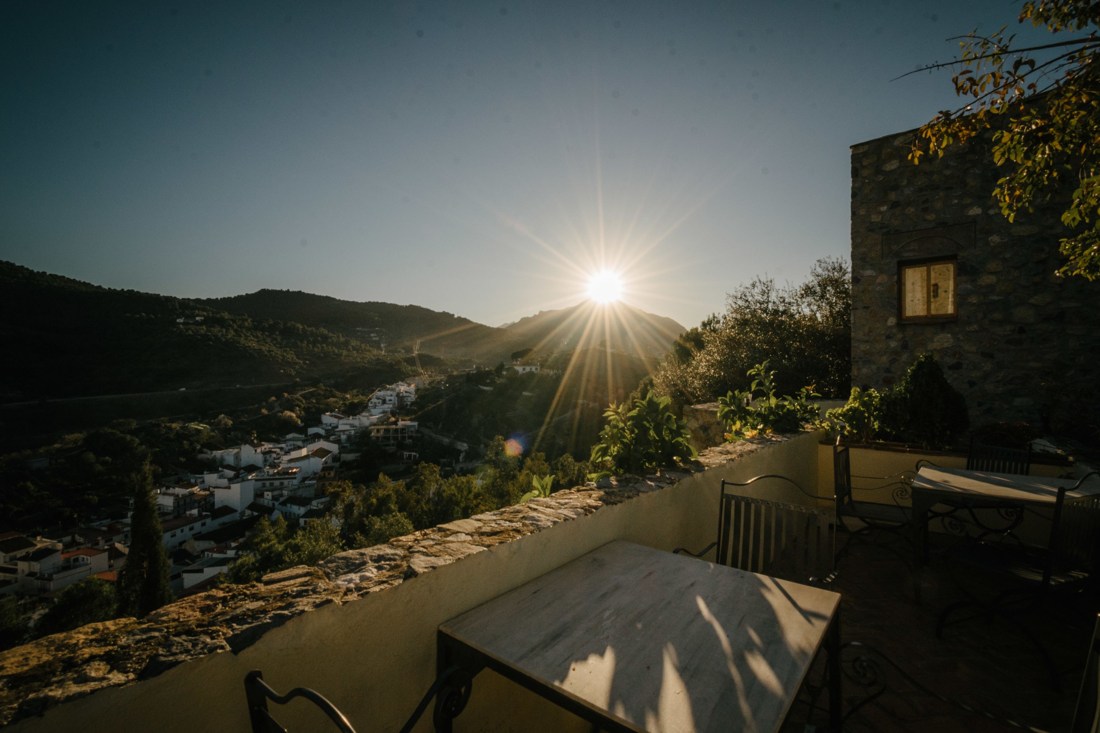 Une terrasse avec une table et des chaises, donnant sur une vallée parsemée de bâtiments et de collines.