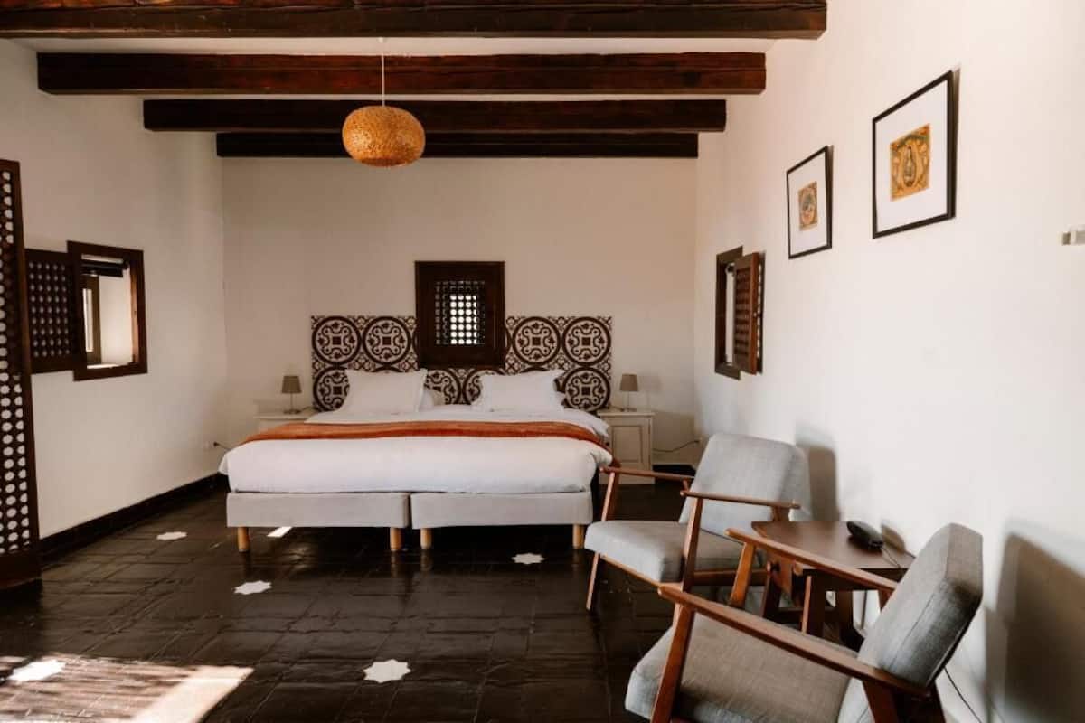 Ein Schlafzimmer mit einem großen Bett, zwei Nachttischen, einer Hängelampe und einem Sessel.