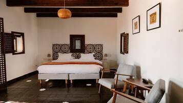 A bedroom with a large bed, two bedside tables, a hanging light fixture, and a chair.