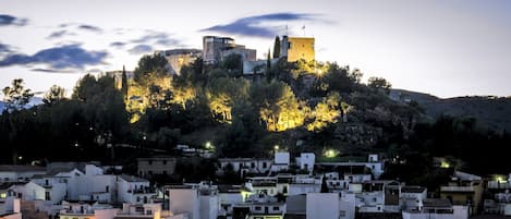 A historic town with a prominent castle on a hill, surrounded by white buildings and lush greenery.