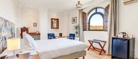 A hotel room with a bed, desk, chairs, a small table, and a view of the desert.