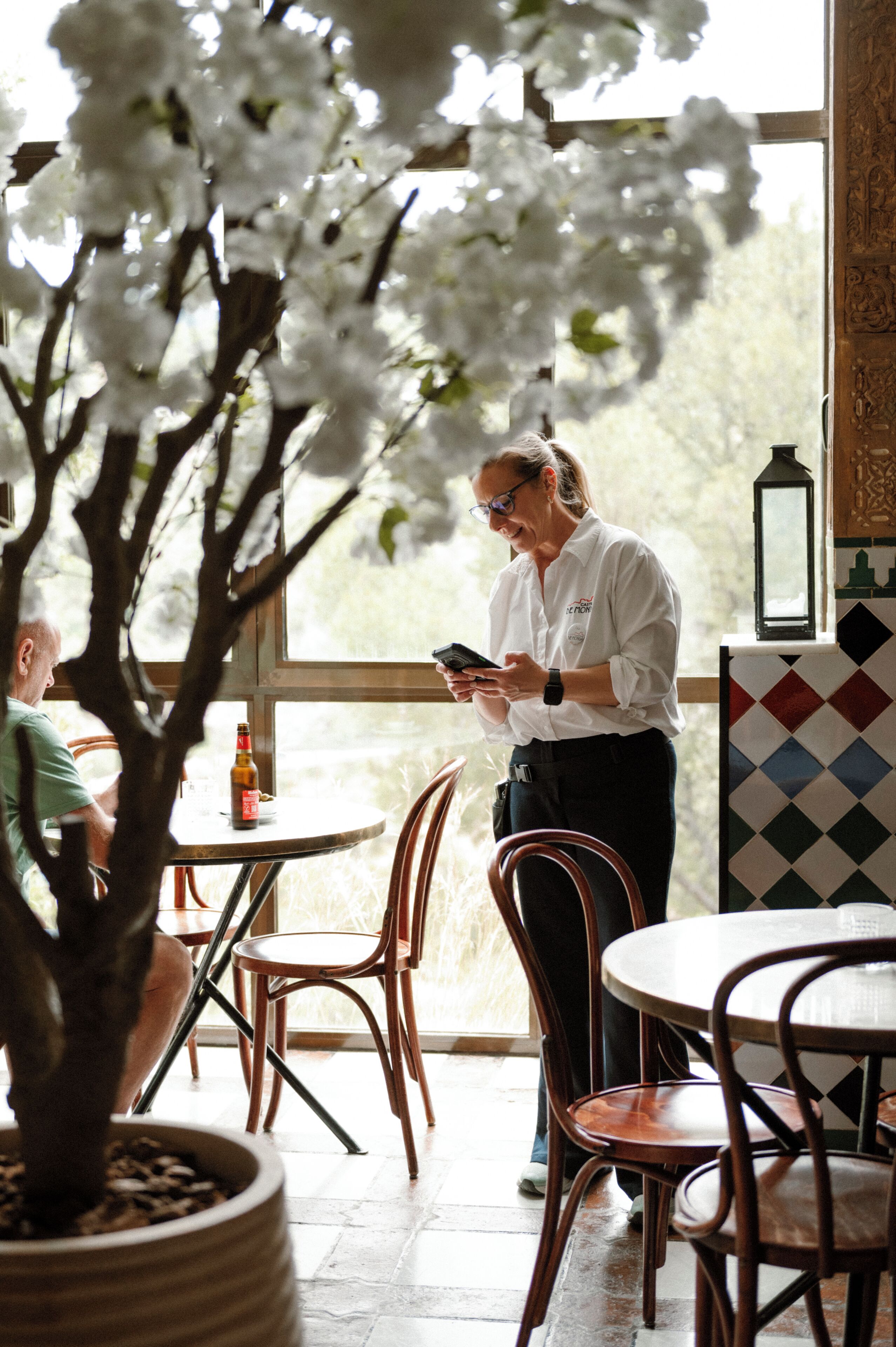Une personne se tient debout près d’une table sur laquelle se trouvent un téléphone intelligent, une plante en pot et une bouteille de bière.
