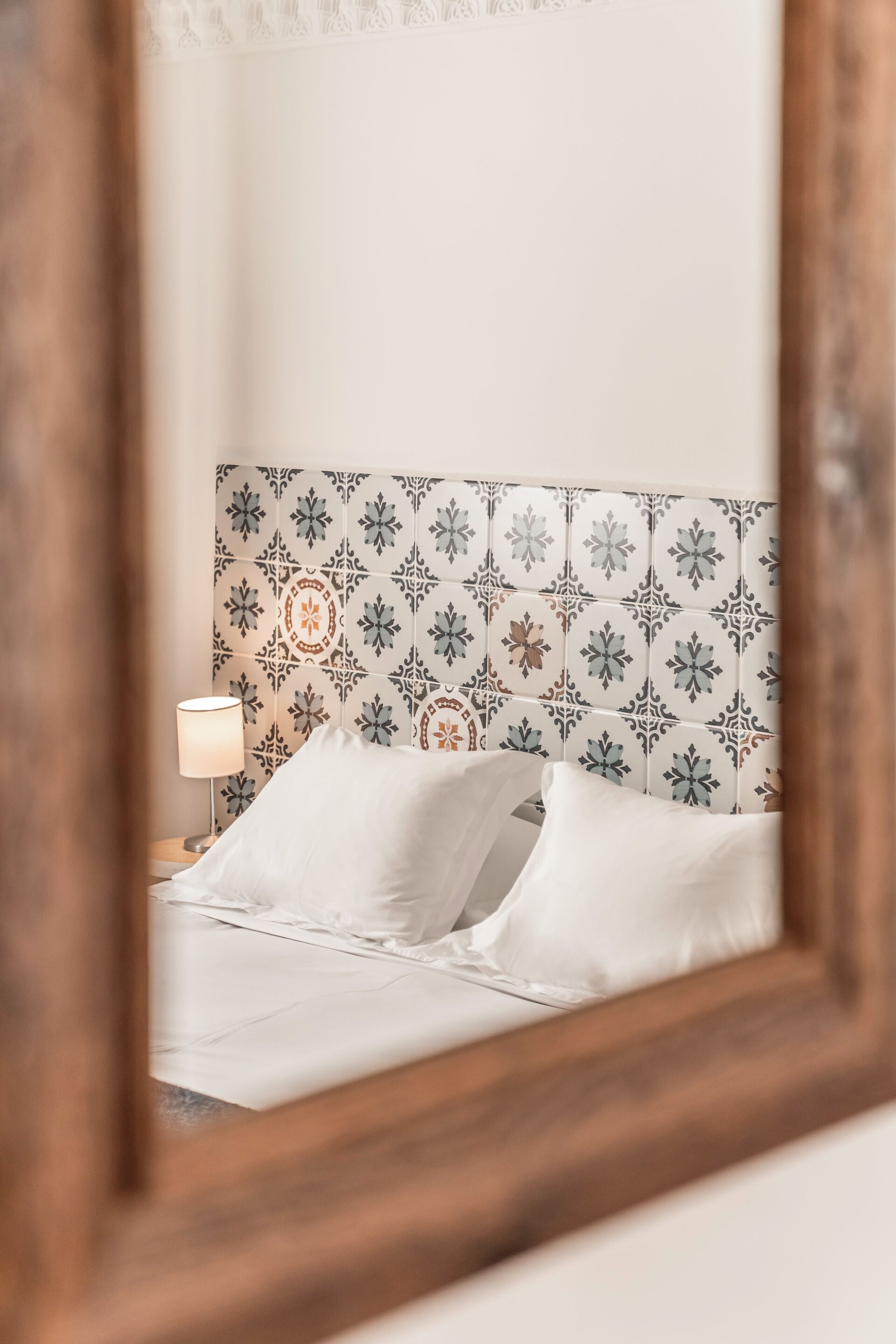 A bedroom with a patterned headboard, a bedside lamp, and white bedding.