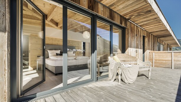 Terraza de madera con un dormitorio acristalado que incluye una cama, una silla y una mesa.