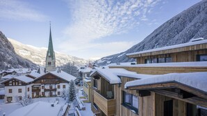 Un pueblo cubierto de nieve con edificios de madera, una iglesia con aguja verde y montañas al fondo.
