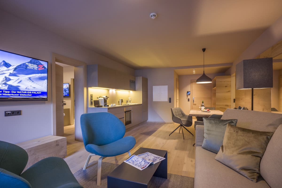 A modern living room with a flat-screen TV, a sofa, a coffee table, and a dining area with a table and chairs.