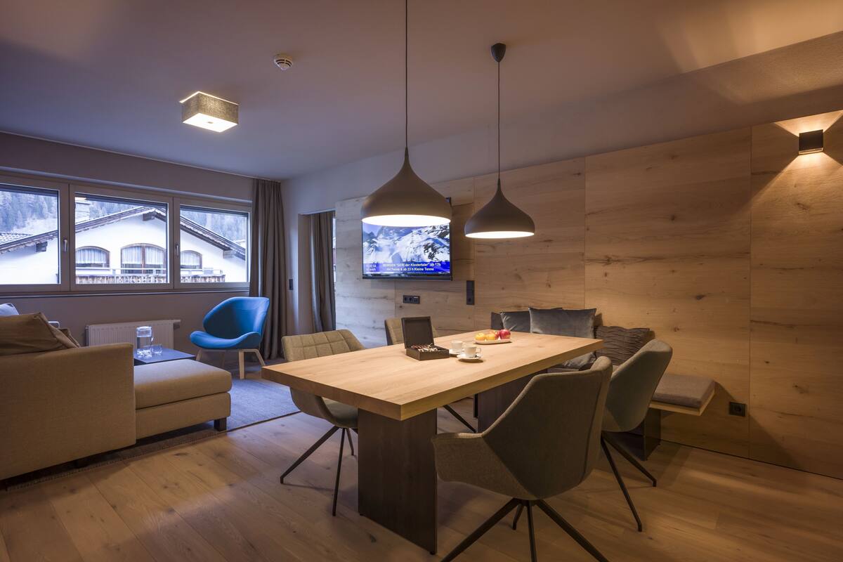 A modern living room with a wooden dining table, grey chairs, a blue armchair, and a television mounted on the wall.