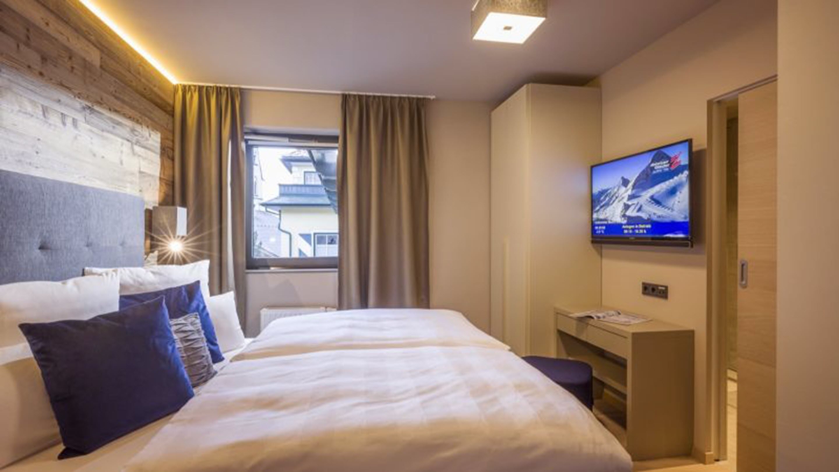 A hotel room with a bed, a desk, a TV, and a window with curtains.