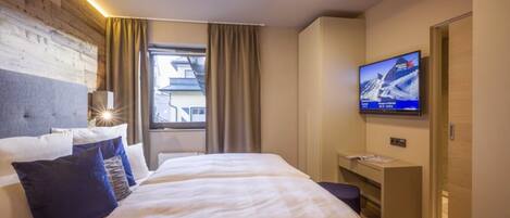 A hotel room with a bed, a desk, a TV, and a window with curtains.