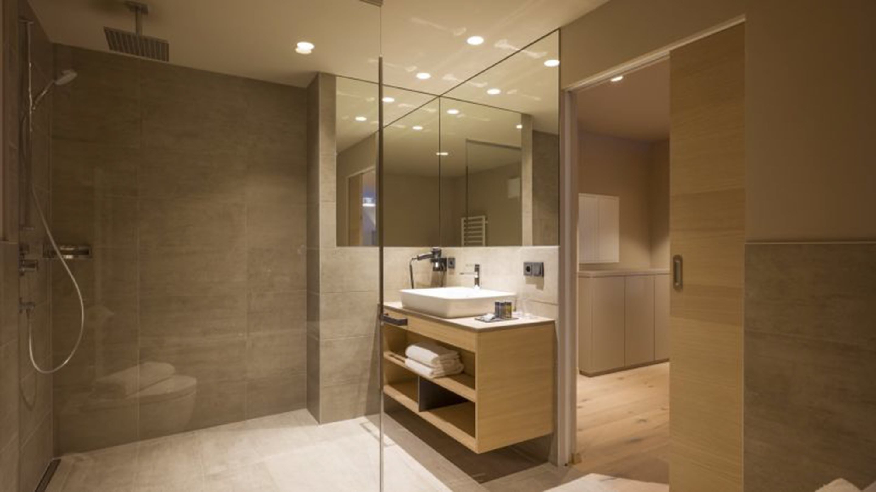 A modern bathroom with a glass shower enclosure, a wooden vanity with a sink, and a large mirror.