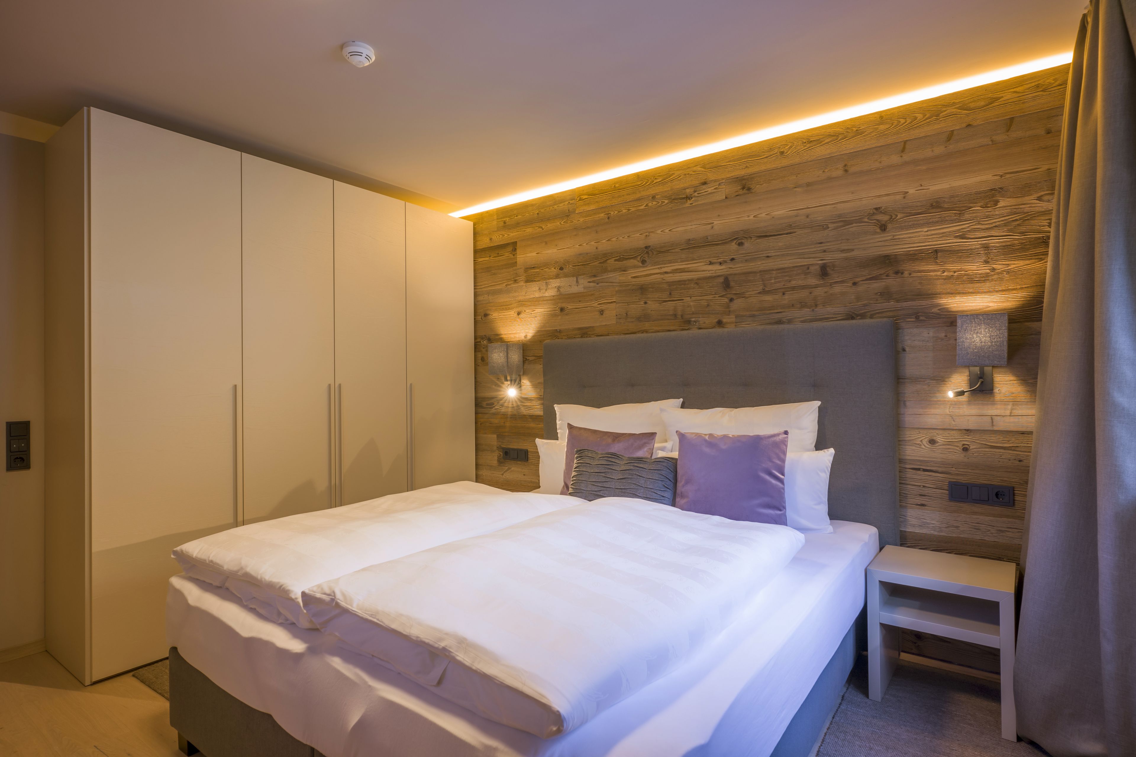 A modern bedroom with a large bed, built-in wardrobe, and a wooden accent wall.