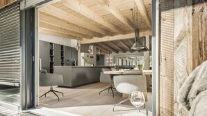Una cocina moderna con vigas de madera, una zona de comedor con mesa de vidrio y un rincón de estar acogedor.