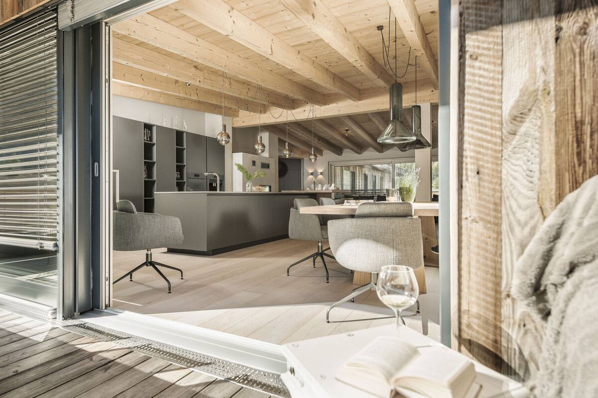 A modern kitchen with wooden beams, a dining area with a glass table, and a cozy seating arrangement.