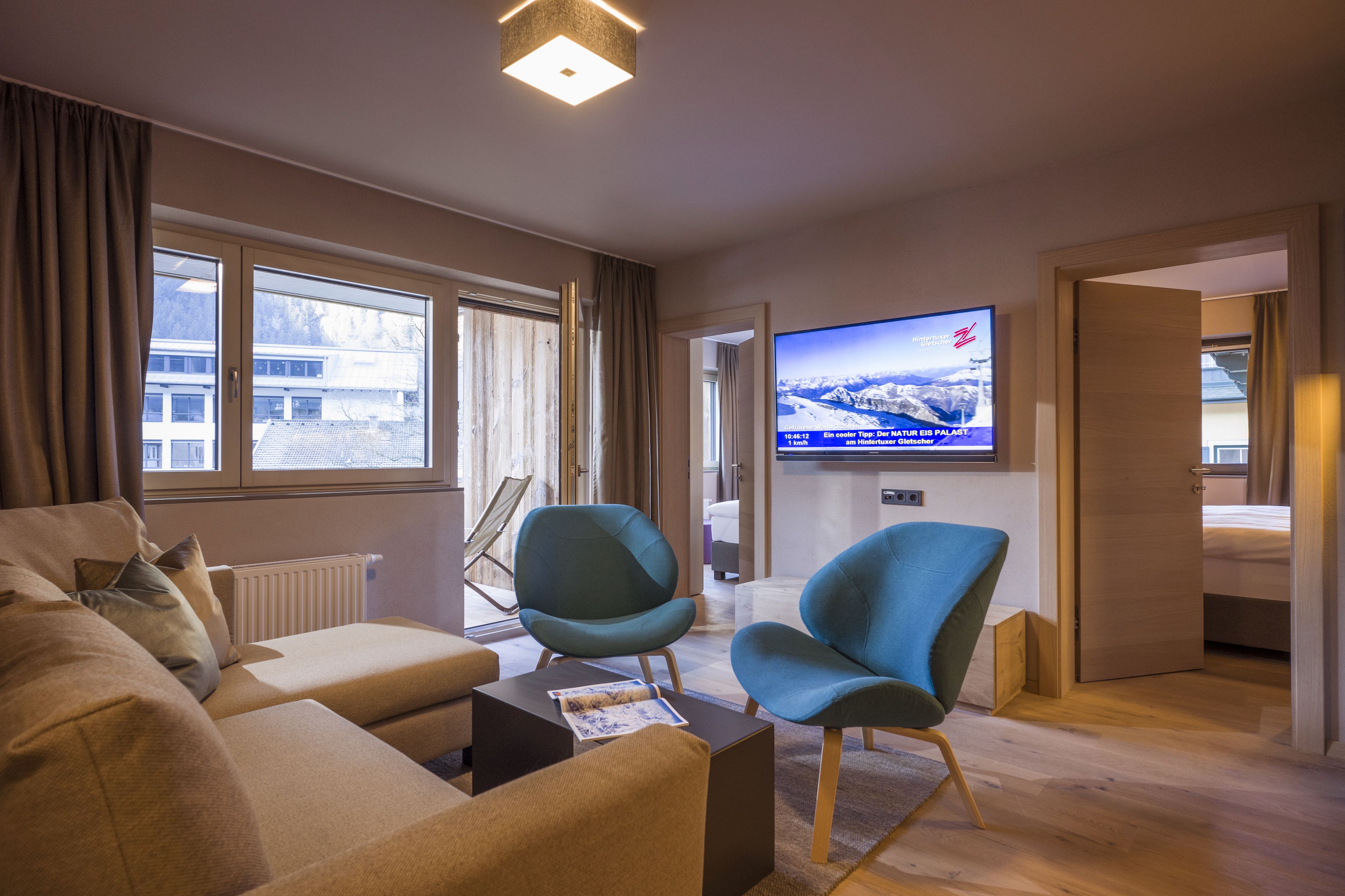 A modern hotel room with a sofa, two chairs, a TV, and a view of a snowy landscape through the window.