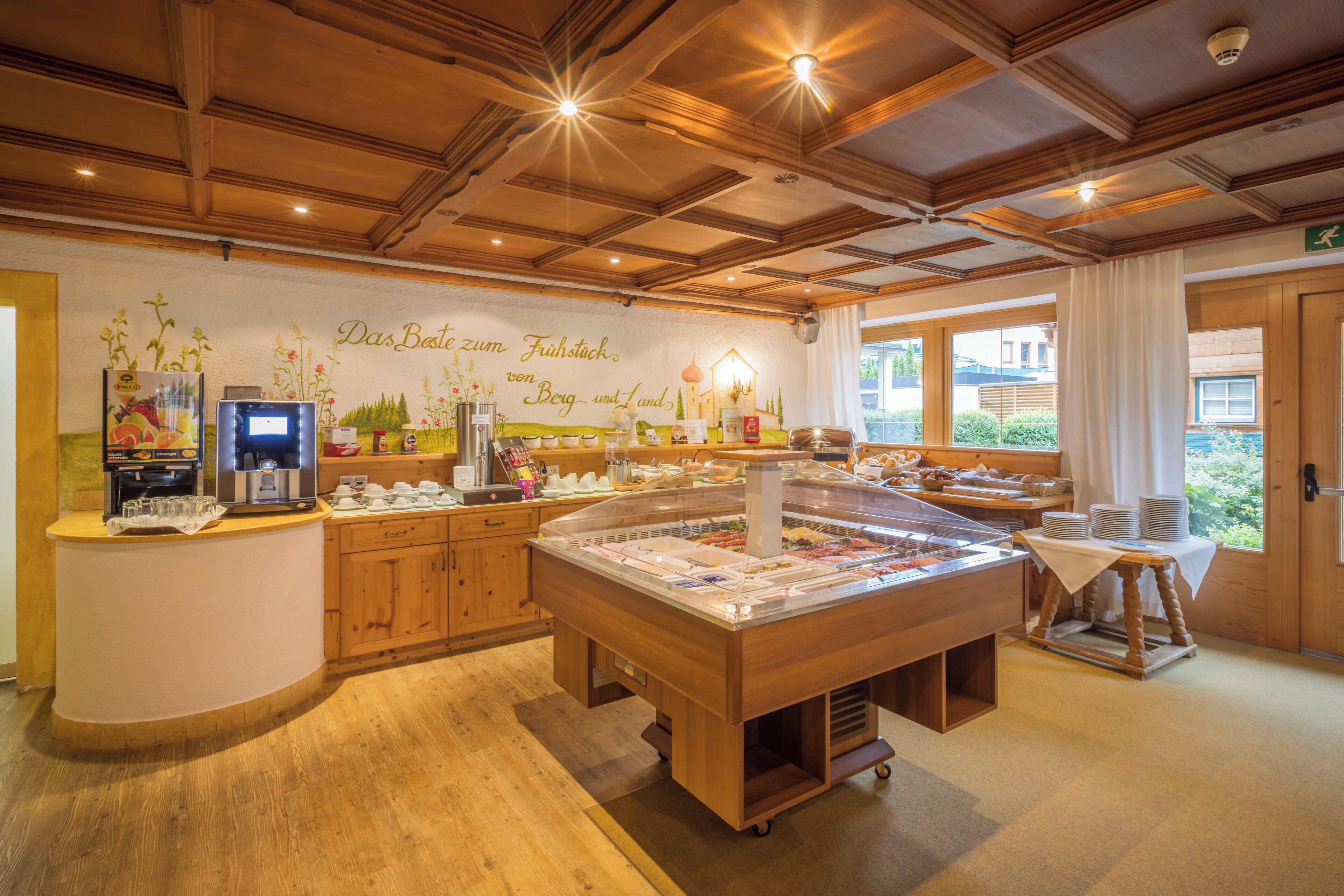 A breakfast buffet area with wooden cabinets, a coffee machine, and a wall mural.