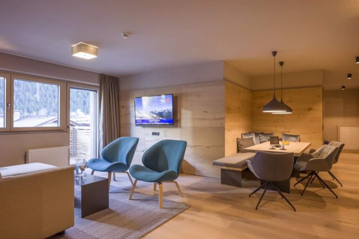 A modern living room with a sofa, two armchairs, a coffee table, and a dining area with a table and chairs.