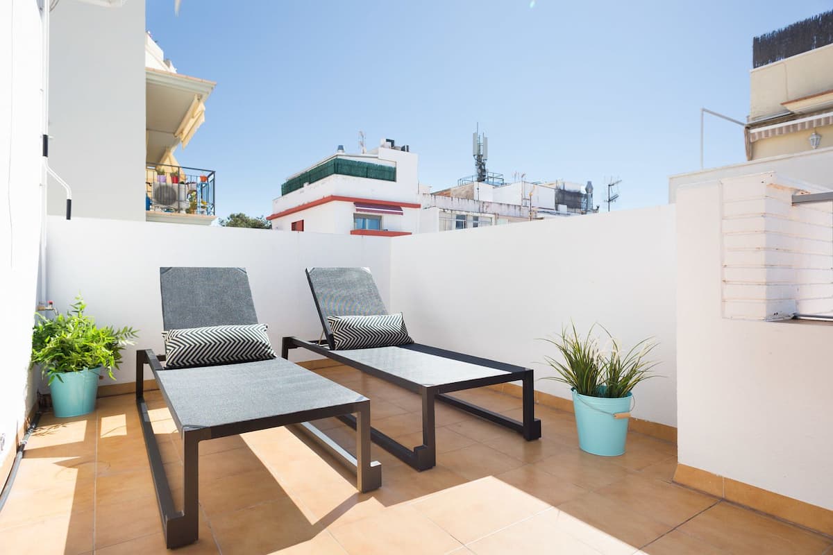 A rooftop terrace with two lounge chairs and potted plants.