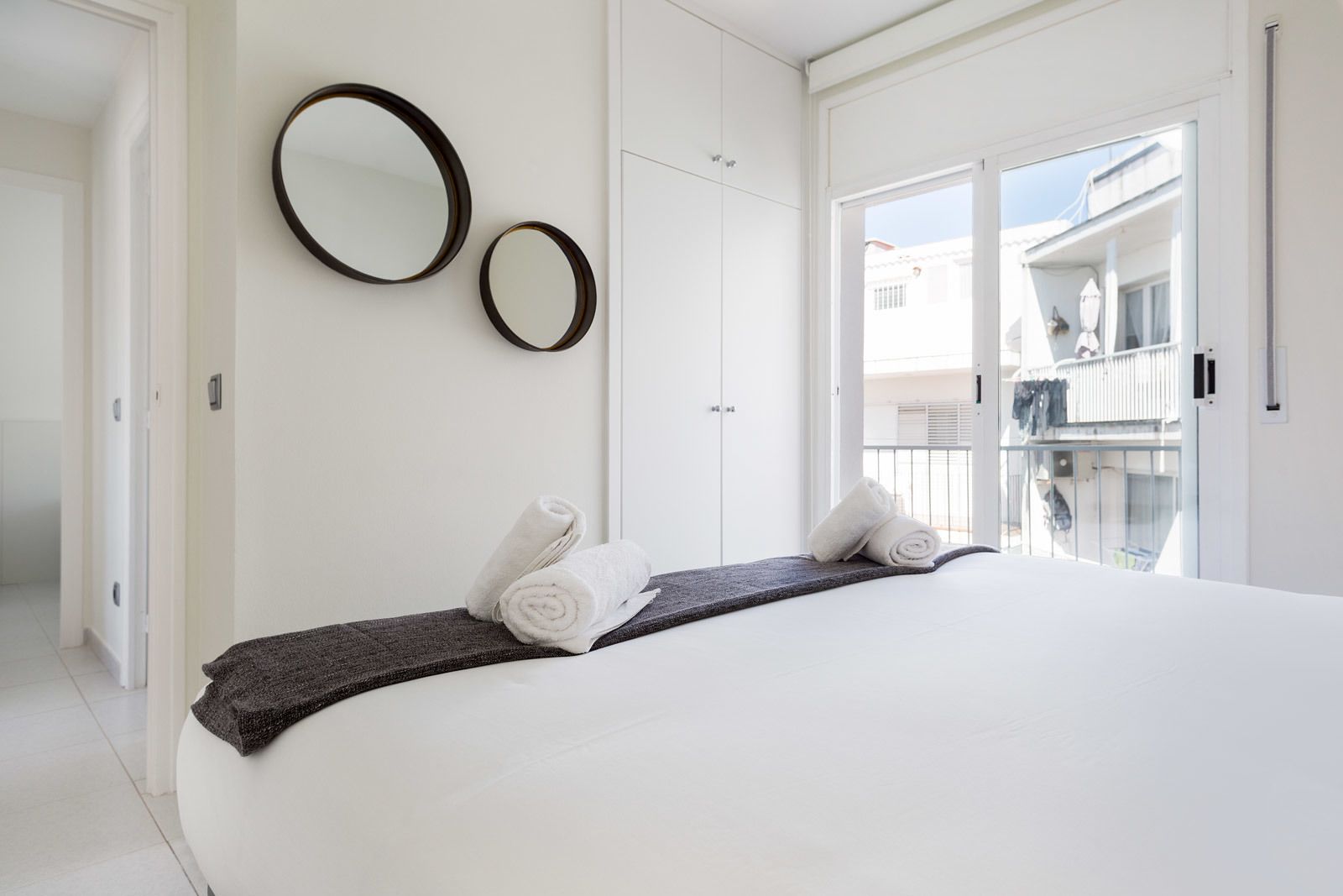 A hotel room with a large bed, two wall mirrors, and a balcony with a view.