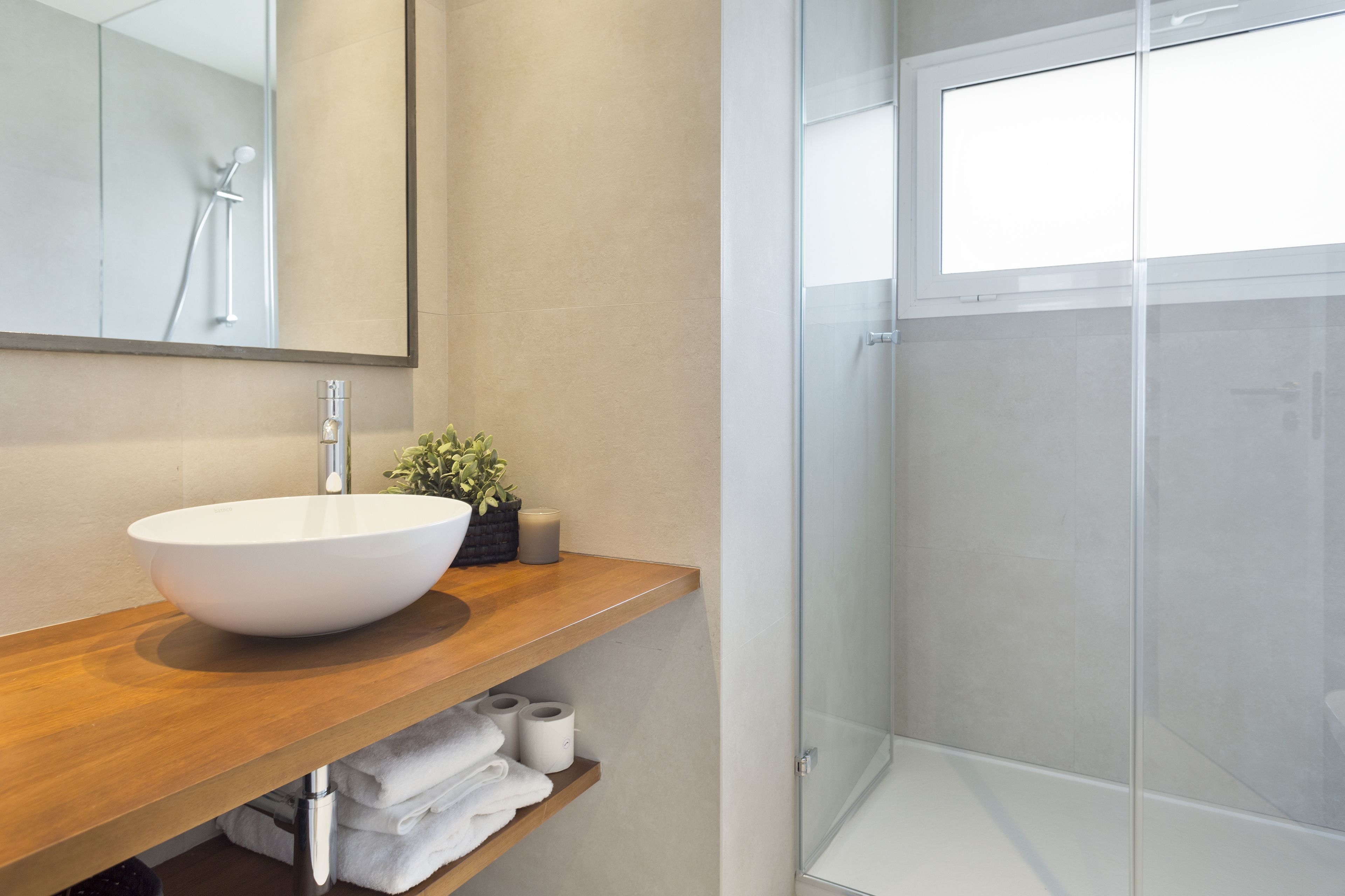 Een moderne badkamer met een groot wit wastafel, een douchecabine van glas en een houten wastafelmeubel.