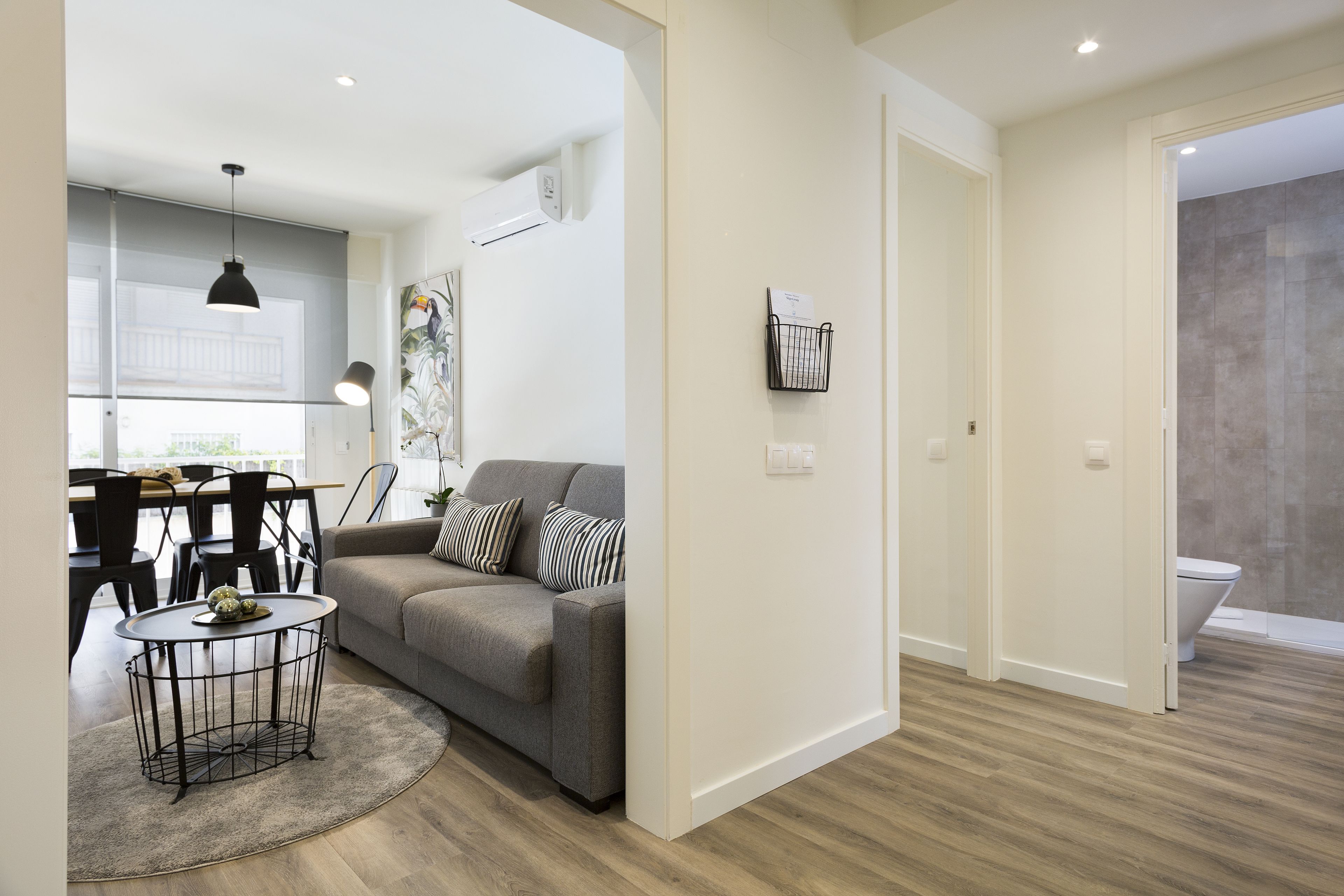 A modern living room with a grey sofa, a round coffee table, and a dining area with chairs and a table.