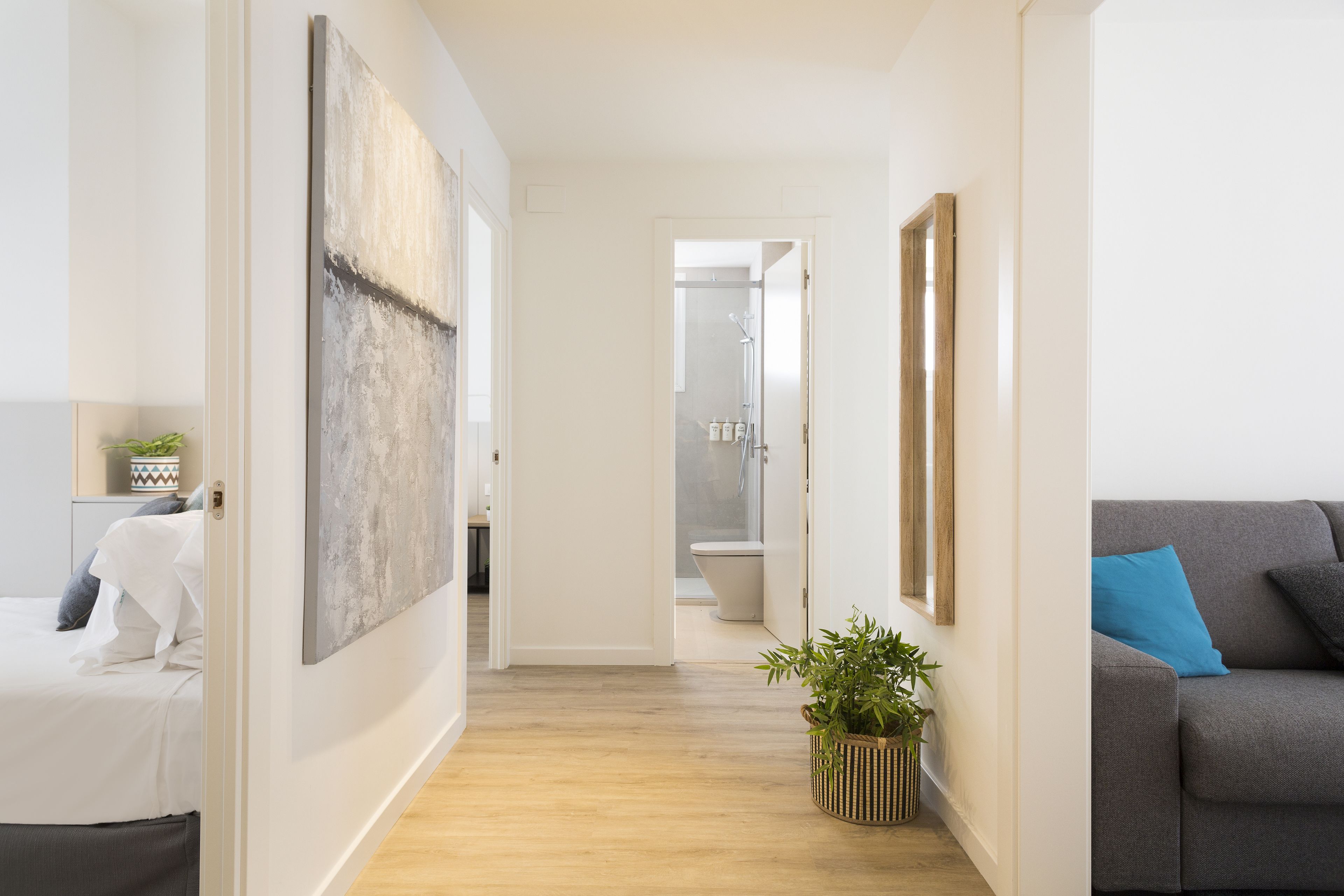 Een moderne woonkamer met een grijze bank, een groot abstract schilderij en een potplant.