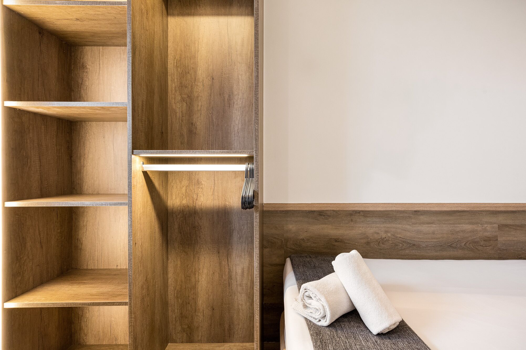 Een hotelkamer met houten planken, een bed met een wit matras en een opgerolde witte handdoek op het bed.
